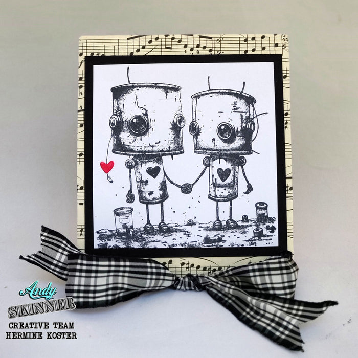 Card with two robots holding hands and a heart, framed with music sheet design and a black and white checkered ribbon.